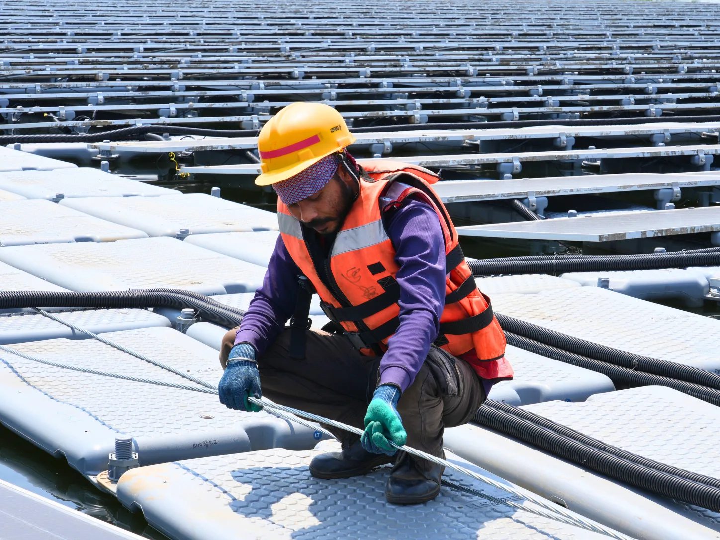 Technician inspecting and tightening a mooring cable on a floating solar array, part of the condition assessment behind end-of-life decisions